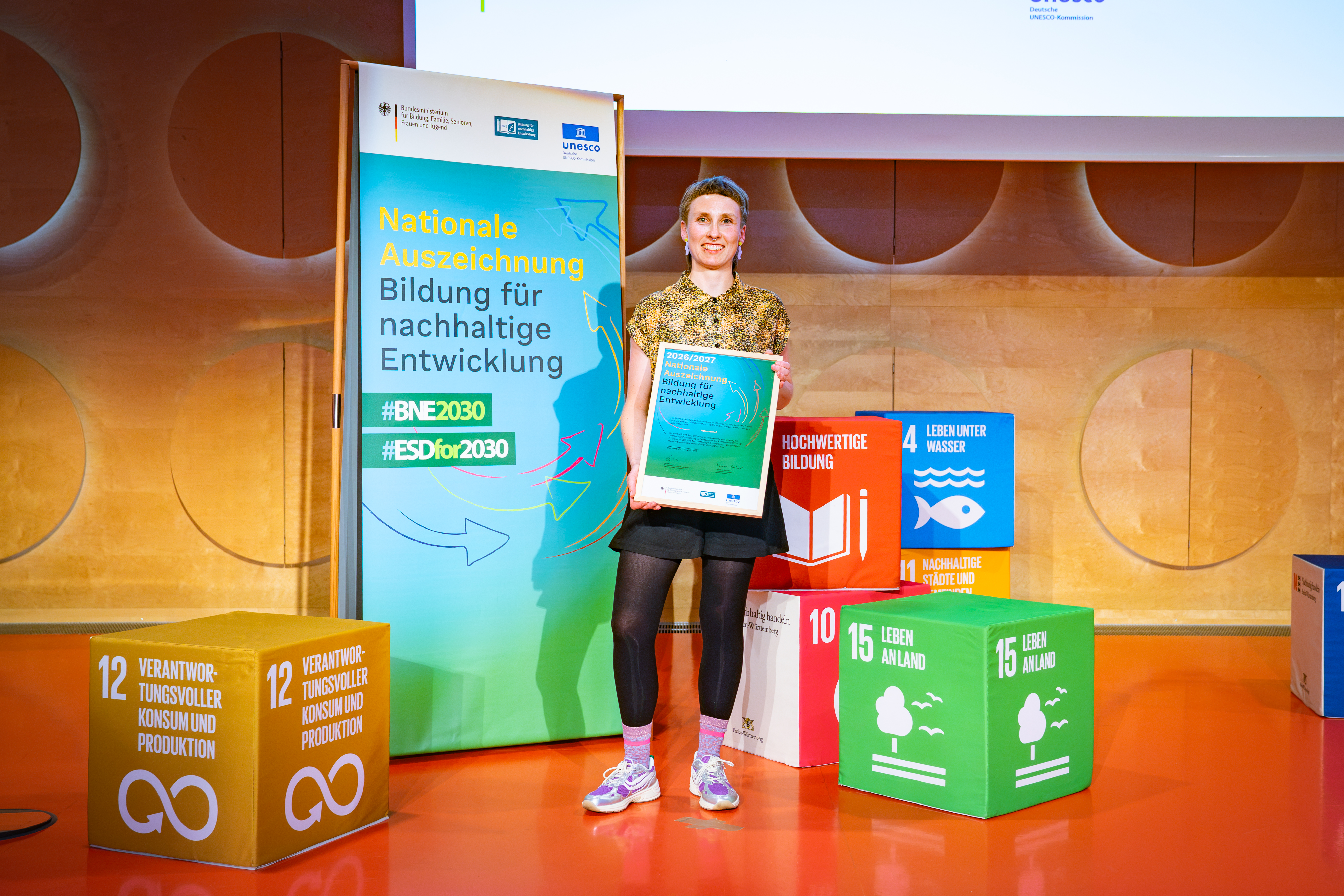 Laura Ziegler mit der Urkunde zwischen SDGs als Kartons