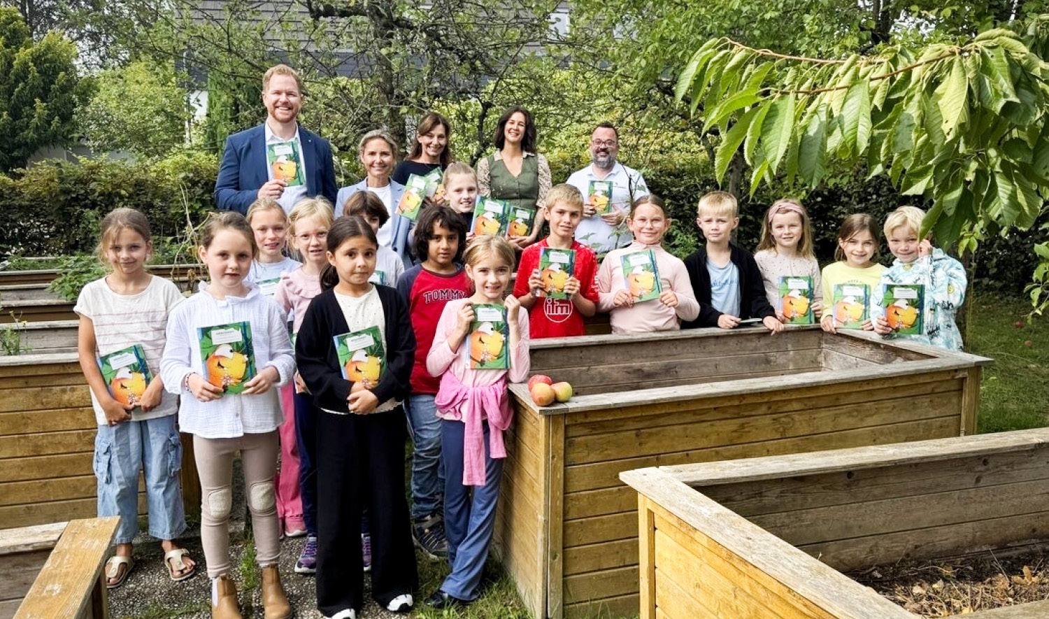 Eine Gruppe Kinder steht mit den Möhrchenheften im Schulgarten, dahinter die Vertreterinnen und Vertreter des Landkreises, der Stadt, der Stabsstelle Klimaschutz und vom Möhrchenheft